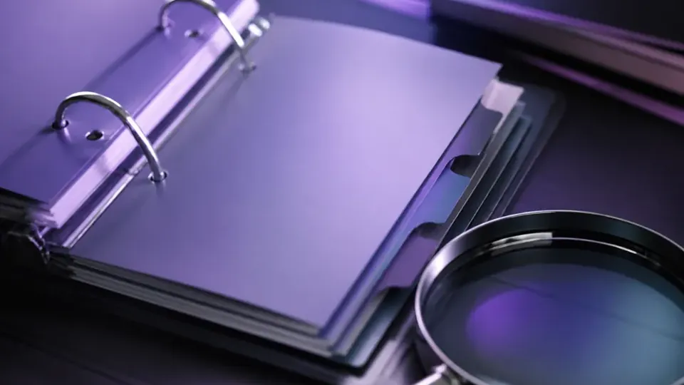 A ring binder with tabbed dividers lies open beside a magnifying glass.