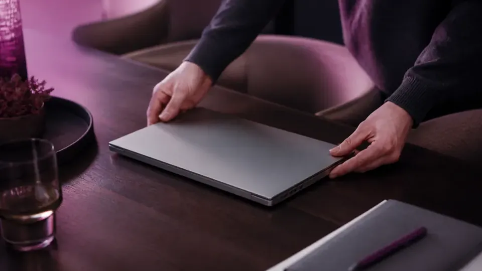 Two hands slide a closed folder across a desk towards someone else.